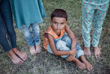 Boy sat wearing the soft orange dino vest in the grass, looking up at the camera