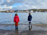Two children facing the water wearing their red and blue jackets.