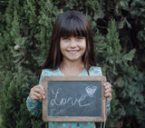 Girl smiling wearing long sleeve aqua fruit splash pyjamas holding a sign that says 'love' on it.