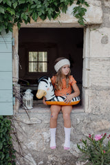 Girl sat wearing short orange dino pyjamas with pool float, on a window ledge.