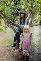 Two girls by a lime tree with one sat in it wearing the long aqua blue fruit splash pyjamas, the other is wearing the pink butterfly reversible dress smiling.