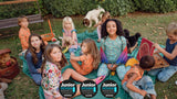 Children sitting outdoors having a picnic eating pizza with 'Junior Design Awards' logo 