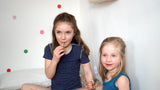 Two girls sit smiling eating sweets wearing the soft short pyjamas in blue leopard, and the tank top in peacock blue.