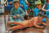 boy wearing a orange dinosaurs print pyjamas in modal playing on the floor with other children in the background