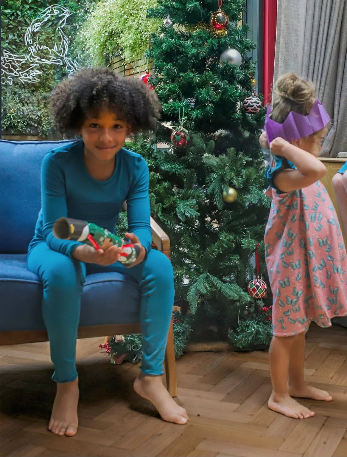 boy smiling by a christmas tree holding a christmas cracker