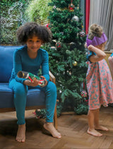 boy smiling by a christmas tree holding a christmas cracker