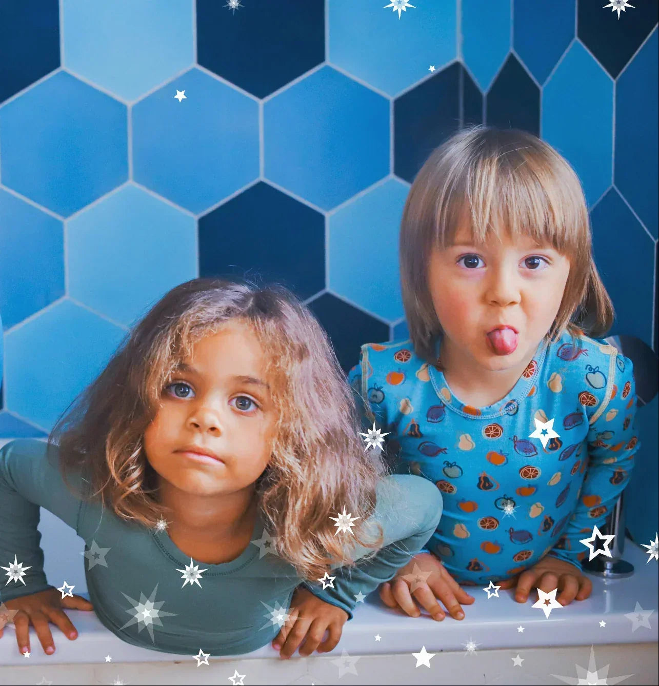 a girl wearing a green long sleeve pyjamas and a boy wearing a turquoise pyjamas with fruit patterns in a bathtub