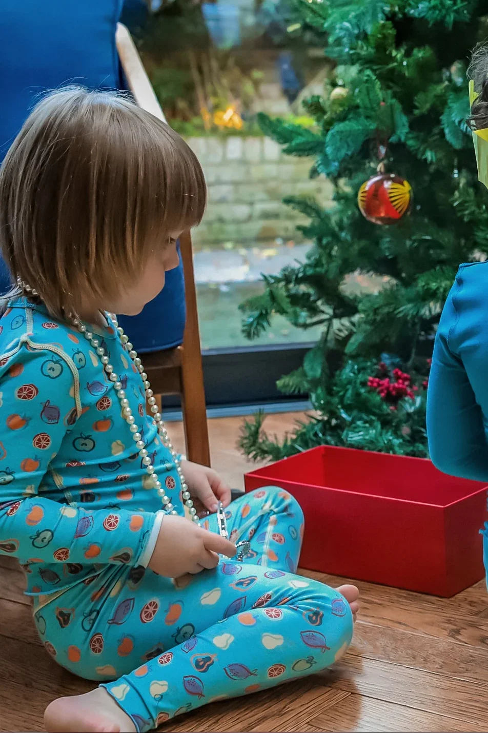 boy playing by a Christmas tree wearing a turquoise pyjamas with fruits on it