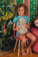 girl with plush toy rabbit wearing a soft short sleeves pyjamas with a turquoise fruit pattern in front of a Christmas tree