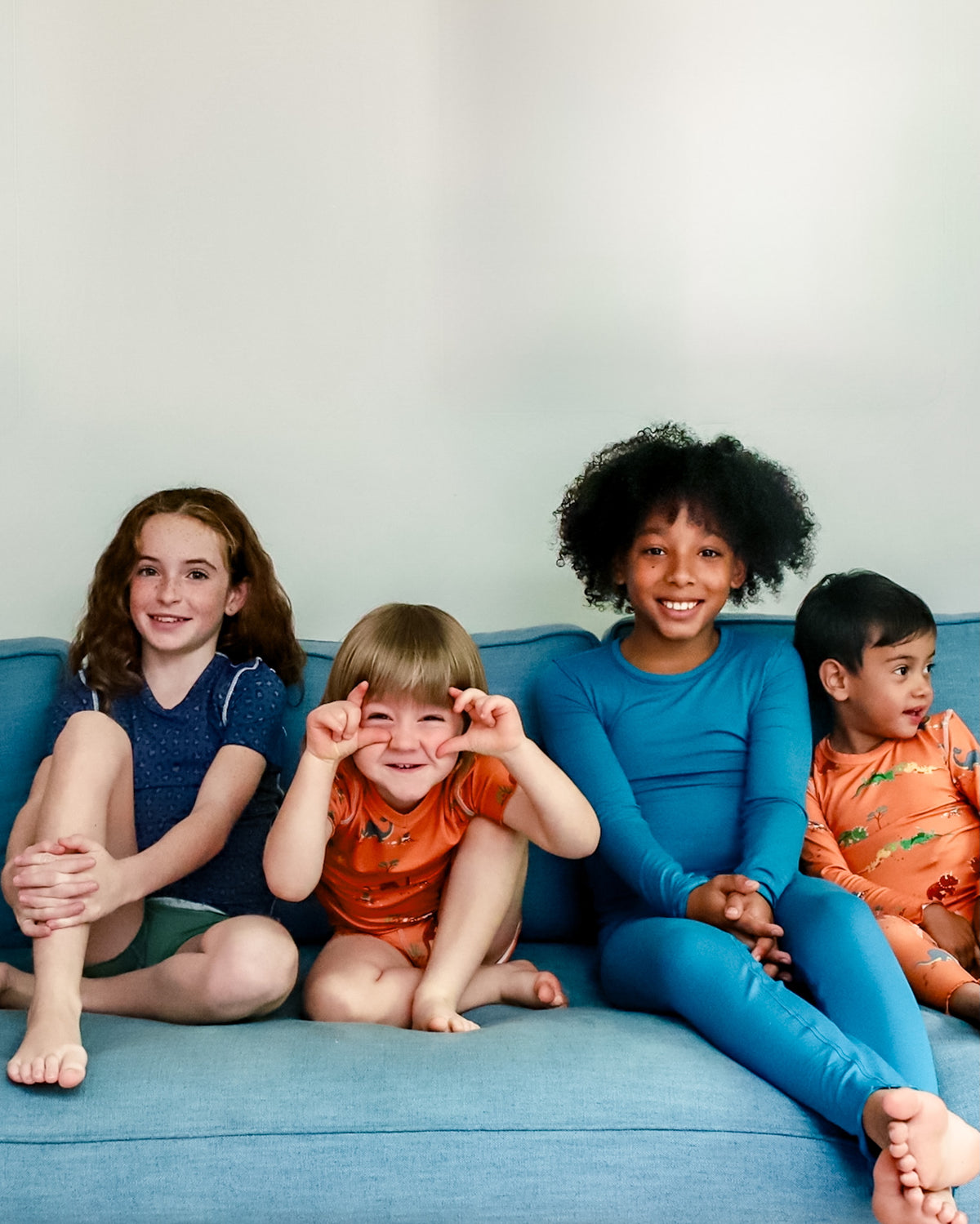 Children smiling sitting close together on a sofa wearing soft, sensory-friendly pyjamas