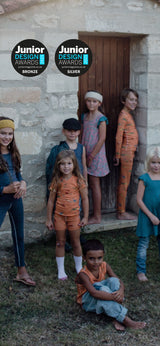 Children in pyjamas standing in front of a stone building with 'Junior Design Awards' logos.