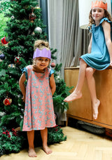 Two children in party hats wearing Morning Marvels sensory-friendly dresses near a Christmas tree